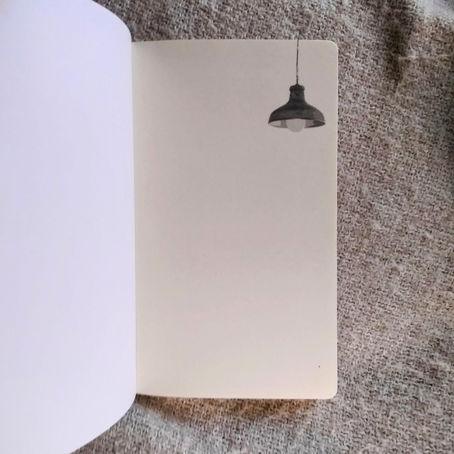 Notebook with a drawing of a hanging light on the right hand page in greyscale, sitting on a textured surface