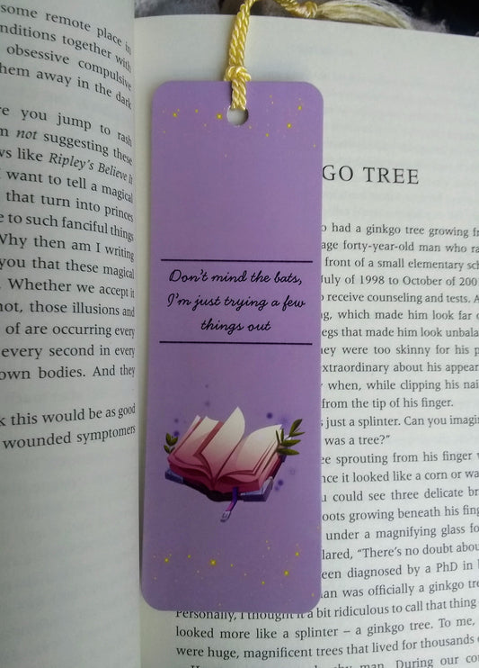 Purple bookmark with the text 'don't mind the bats, I'm just trying a few things out' and a spellbook illustration on an open book
