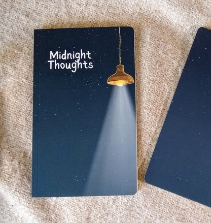 Notebook with 'Midnight Thoughts' on the cover, illustration of a starry night sky illuminated by a hanging lamp, sitting on a textured surface