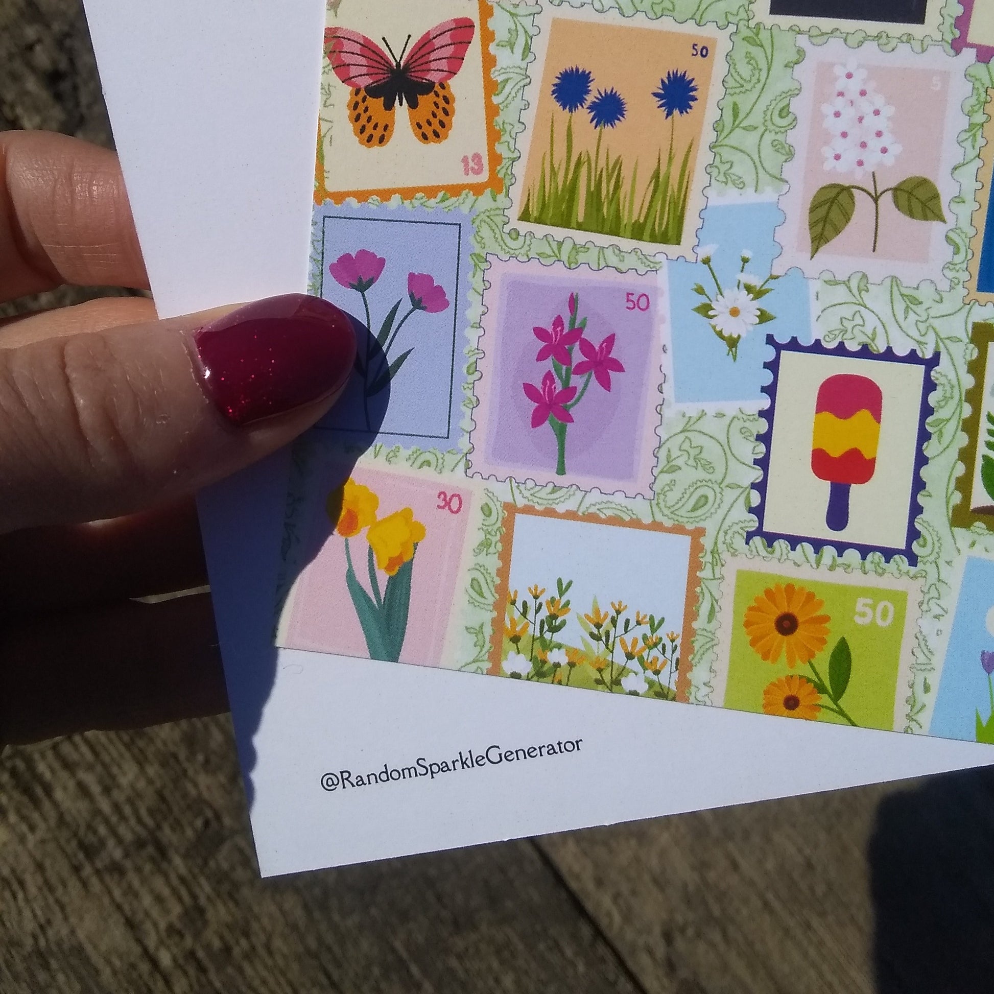 Hand holding a card with colorful postage stamp designs featuring flowers and a butterfly.