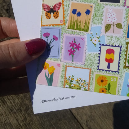 Hand holding a card with colorful postage stamp designs featuring flowers and a butterfly.