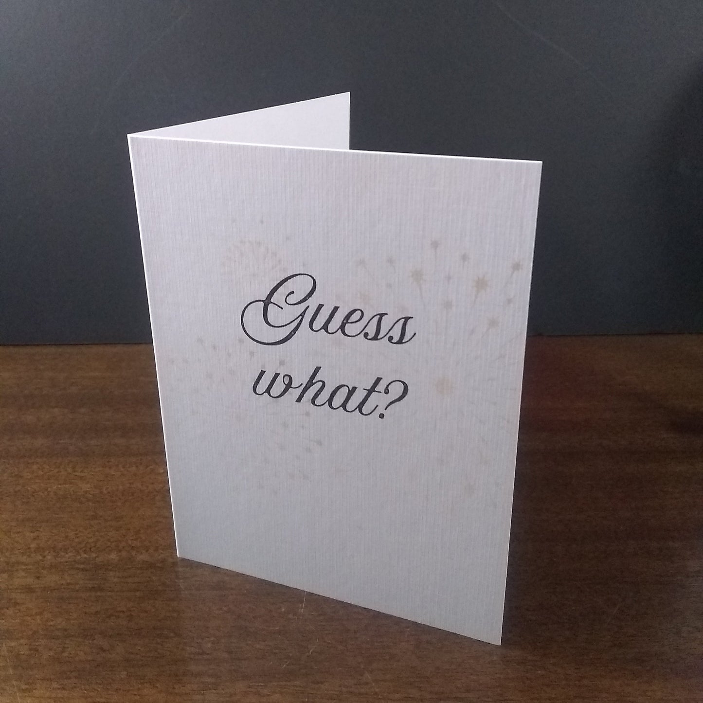 White card with 'Guess what?' text on a wooden surface and dark background