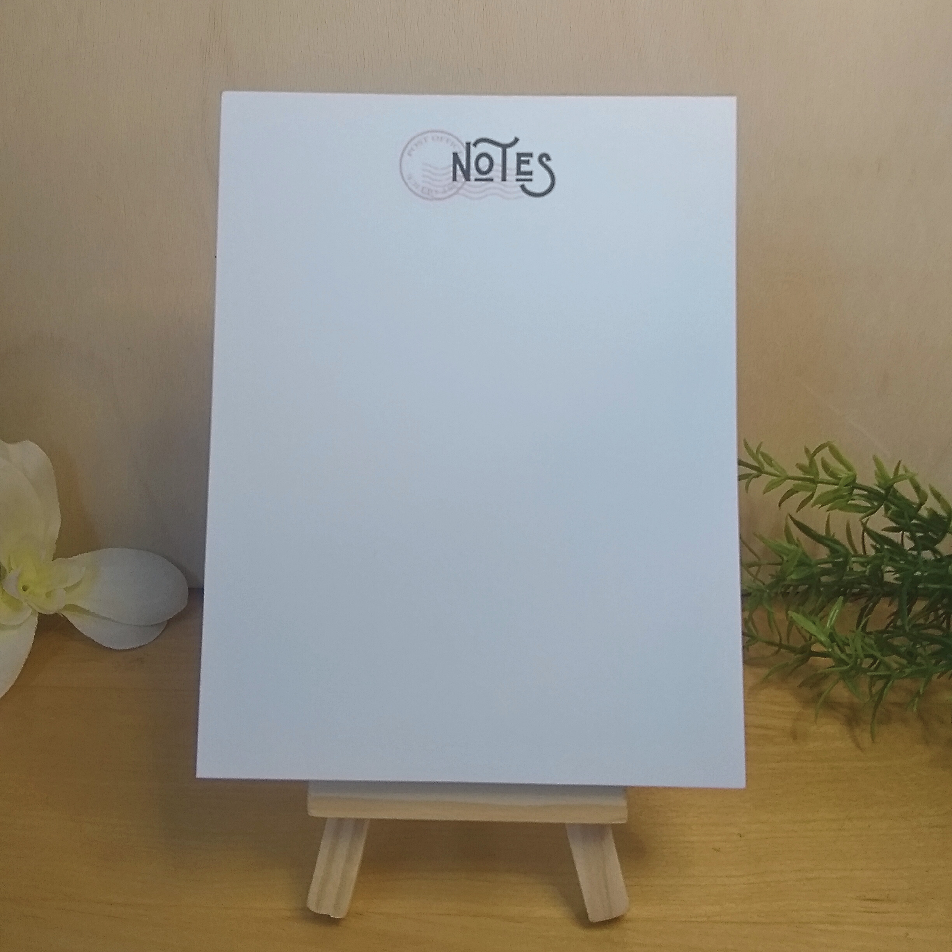 White notepad with 'NOTES' text on a wooden stand against a beige background