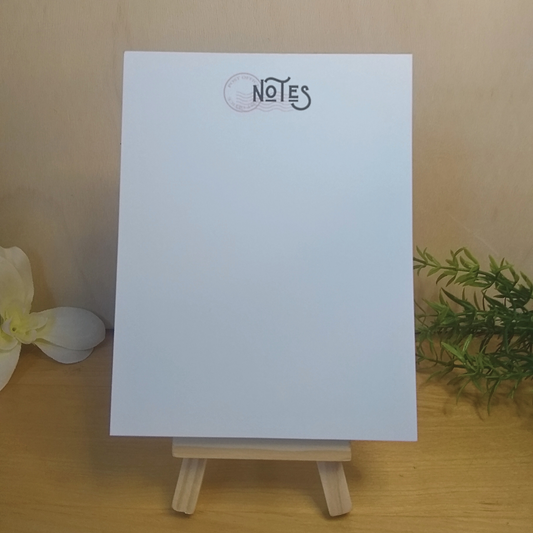 White notepad with 'NOTES' text on a wooden stand against a beige background