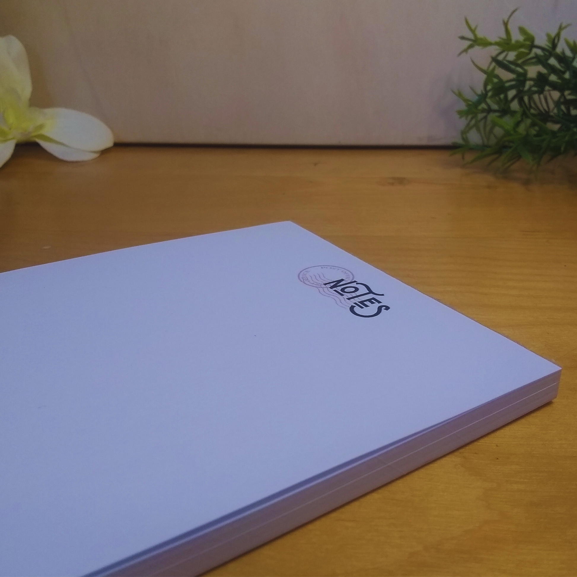 Stack of white notepads with 'NOTES' text on a wooden surface with flowers and plants in the background.